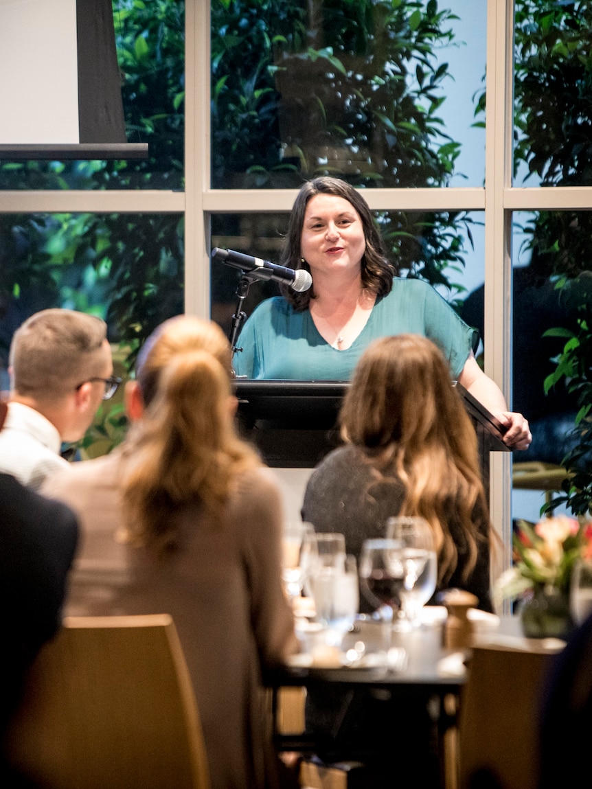 A woman standing at a podium giving a speech as people watch.