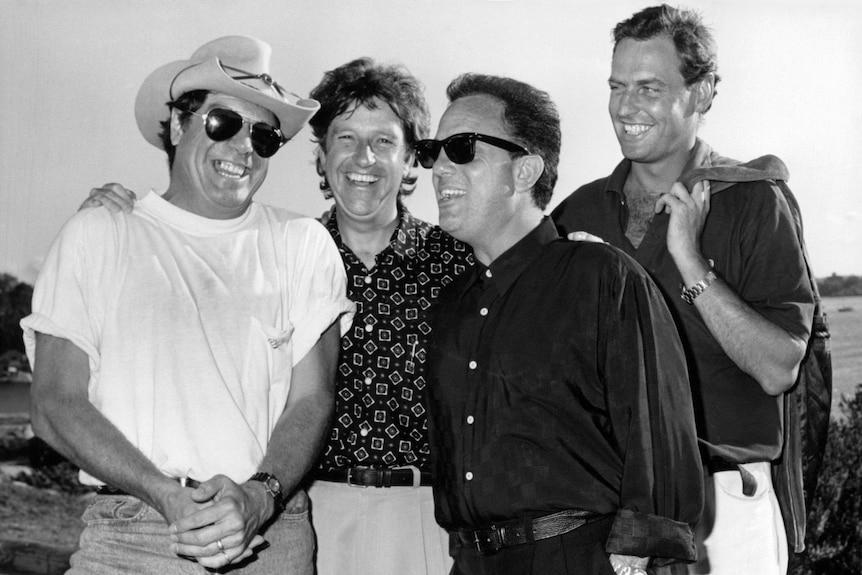 Denis smiles, his hands on the shoulders of Molly Meldrum and Billy Joel. Brad Robinson stands beside Handlin.