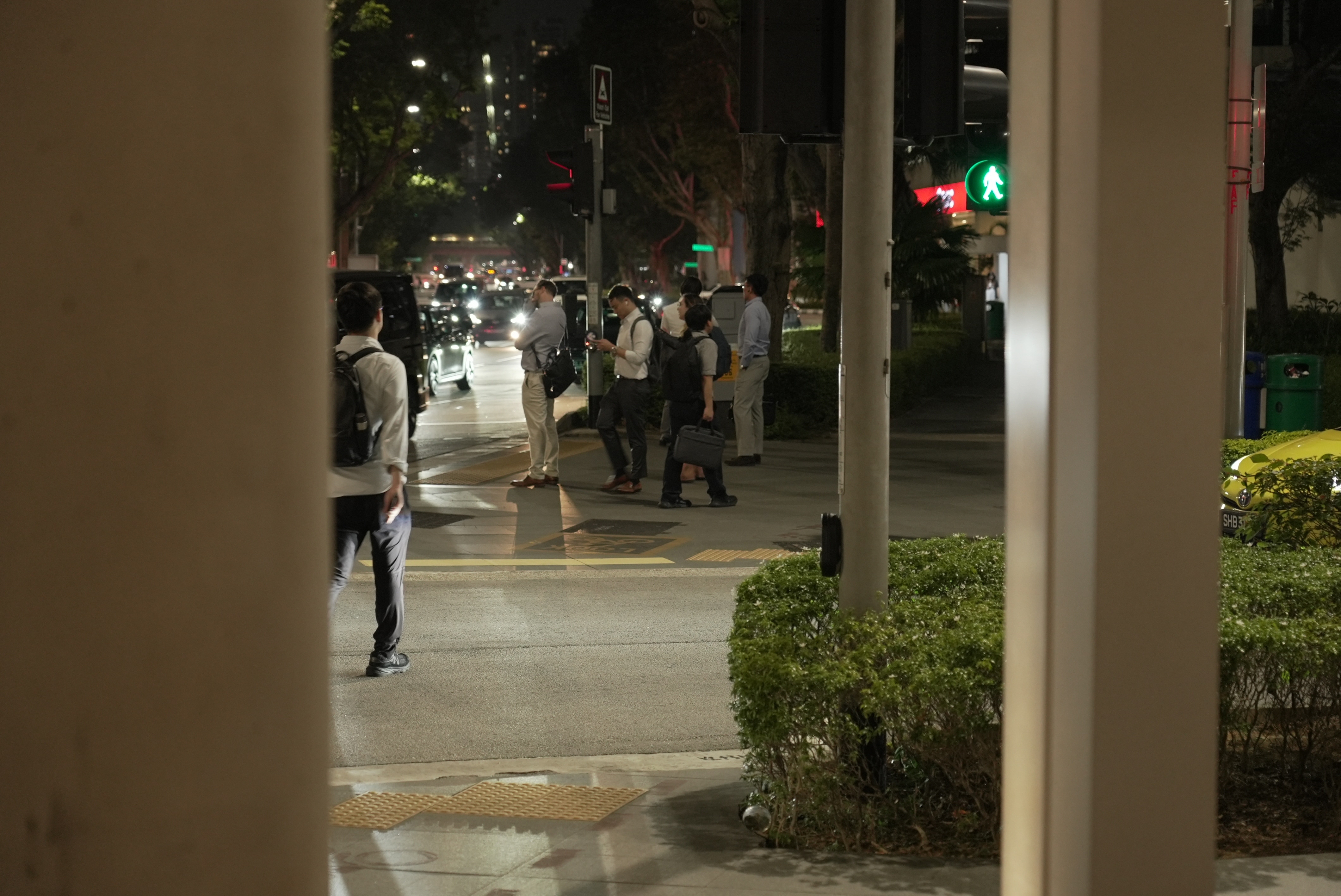A street scape at night, with people standing on a corner.
