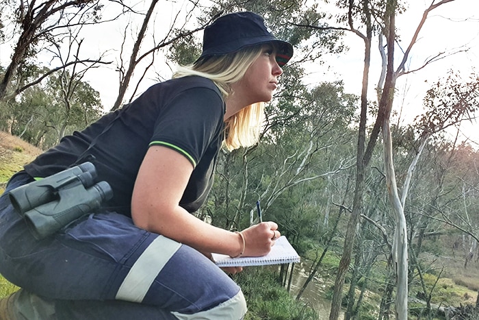 Candice kneeling in the field with notepad and binoculars