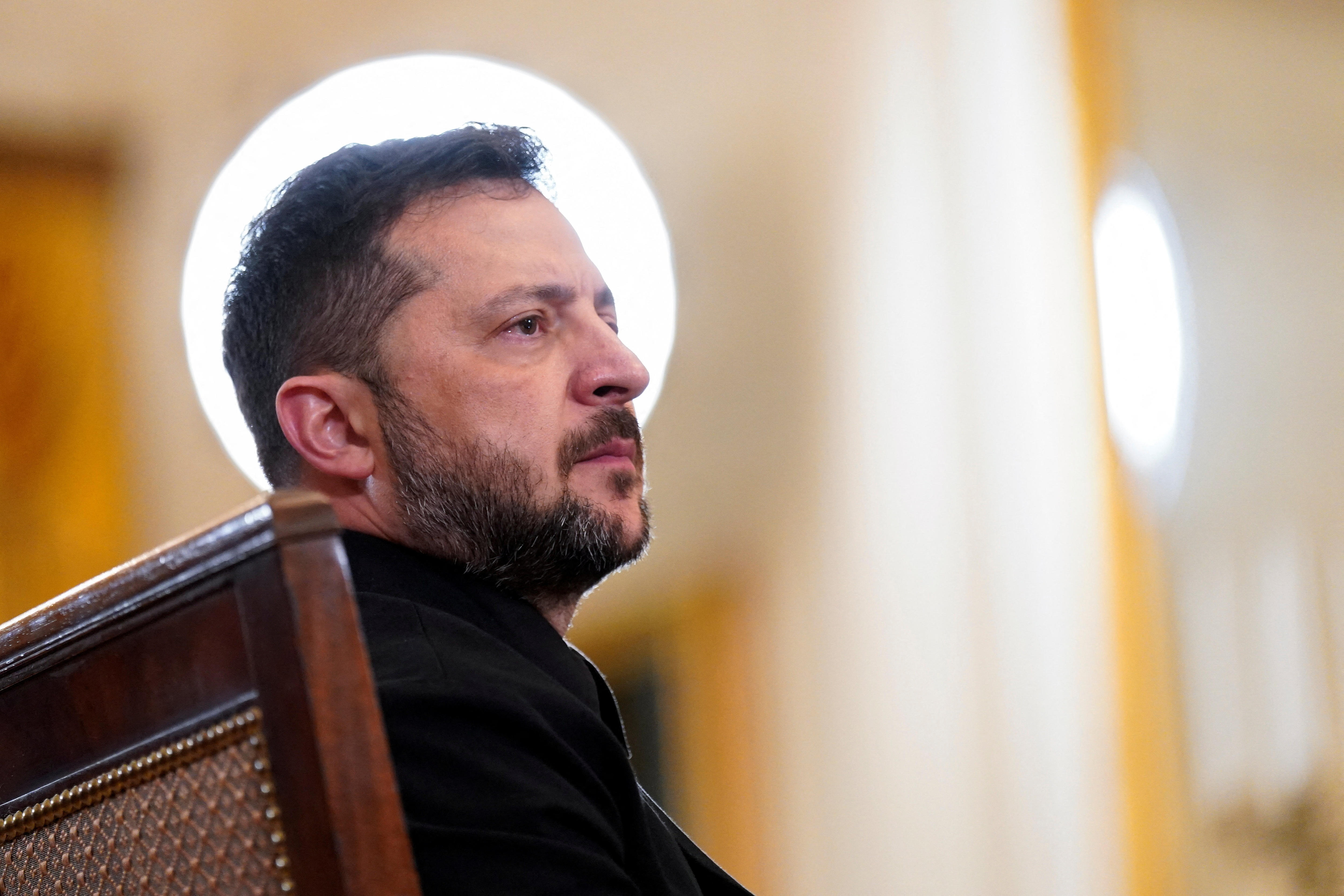 a man sits listening in a room with a light behind his head