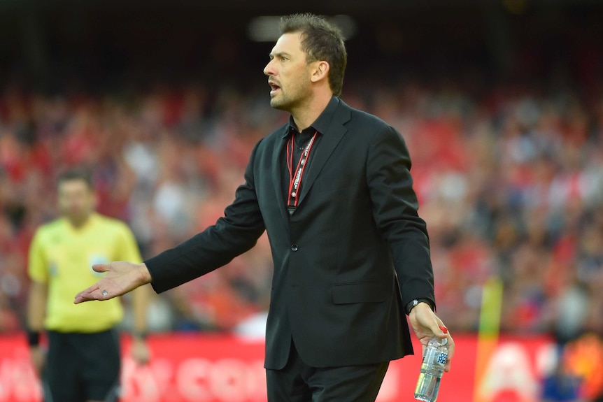 Tony Popovic holds his hands out and looks towards the pitch with a disbelieving look on his face