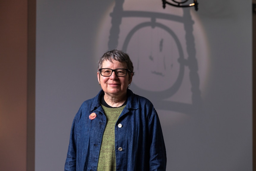 An Aboriginal woman with glasses and grey hair stands in front of projected artwork