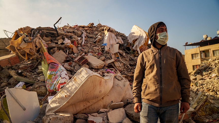 A man in a mask stands in rubble
