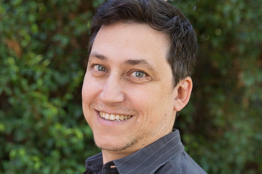 A man smiles for the camera in front of a garden