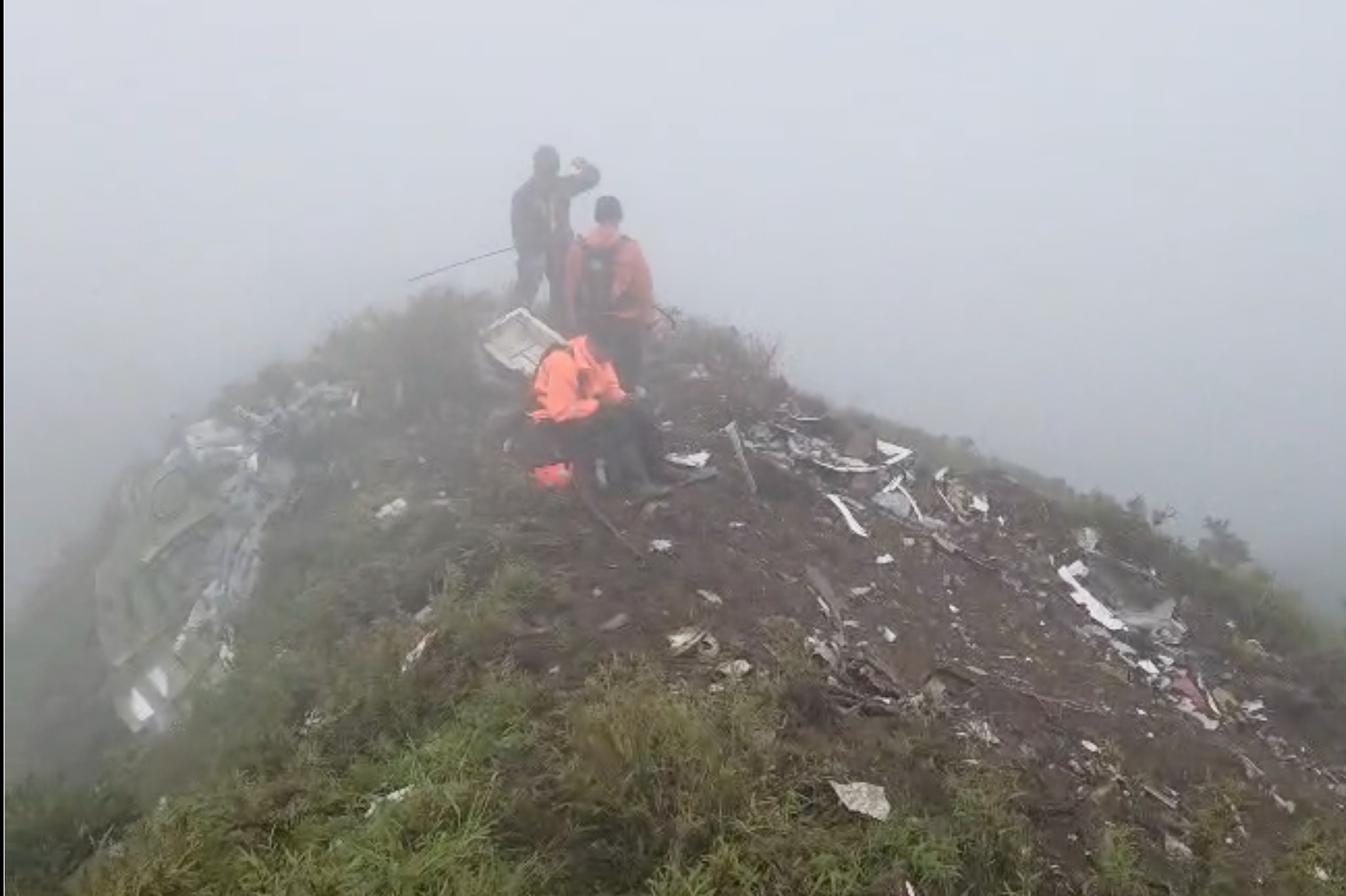 Uma equipe de resgate entre os escombros no topo de uma montanha coberta de nuvens. 
