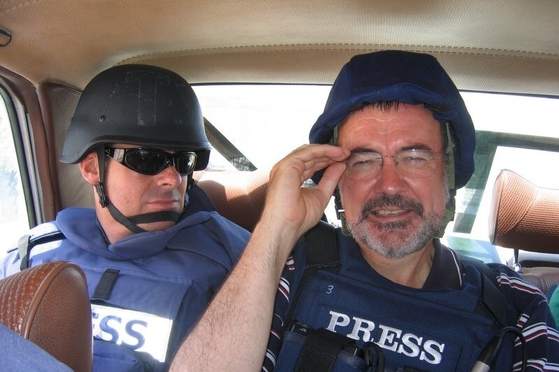 Peter Cave sits in a car wearing body armour and a helmet.