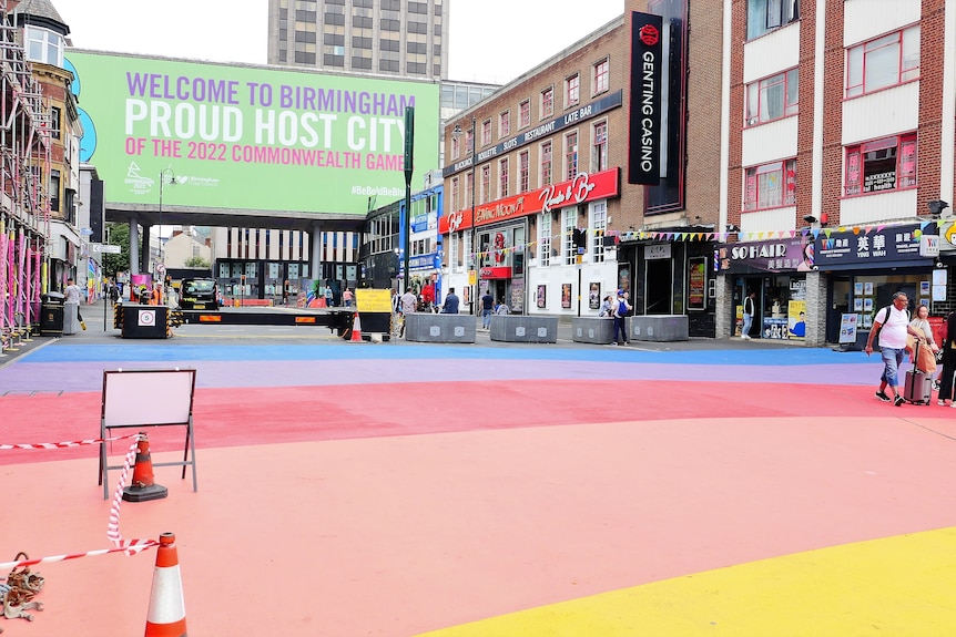 A billboard reads "Welcome to Birmingham, Proud Host CIty of the 2022 Commonwealth Games", a rainbow footpath is in the foreg