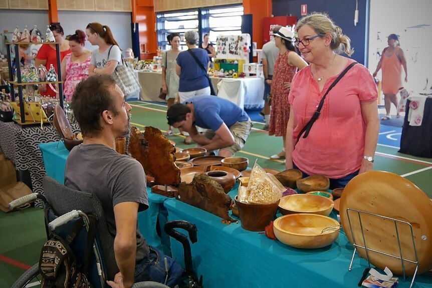Dale Cordwell sits at a market stall of wooden bowls and handmade goods, he is in a wheelchair