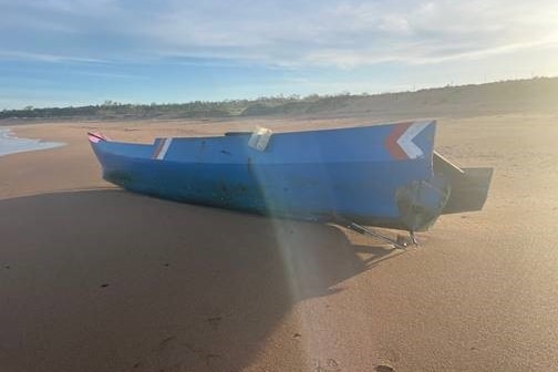 A wooden boat painted pink and blue washed up on a sandy beach