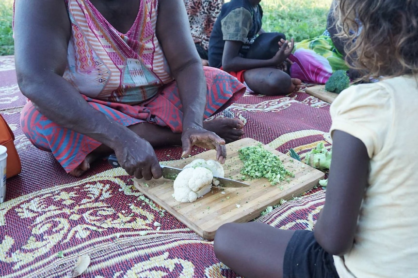 A woman chops vegetables as a child looks on at Elcho Island retreat.