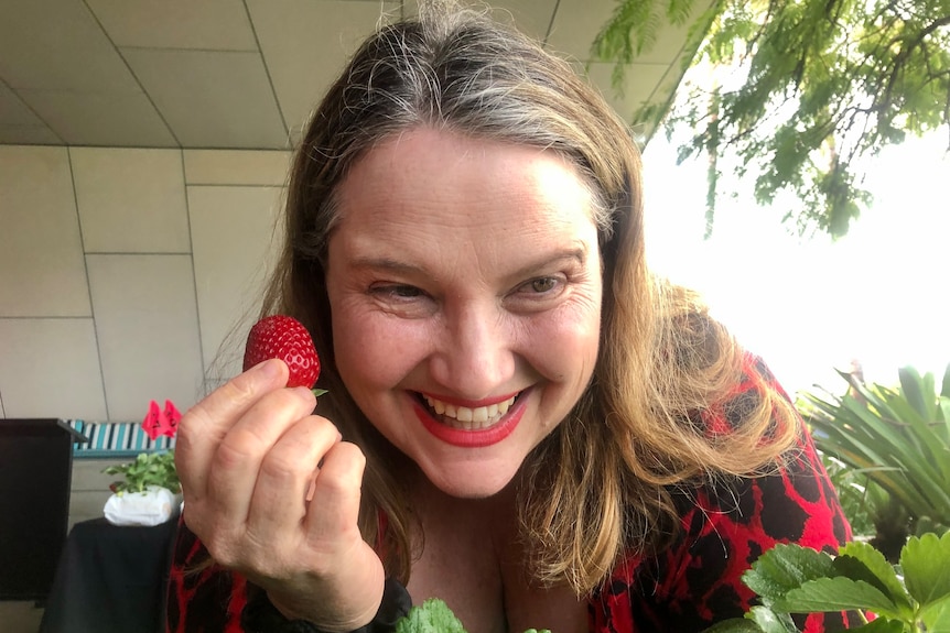 A woman holding a strawberry smiles at the camera