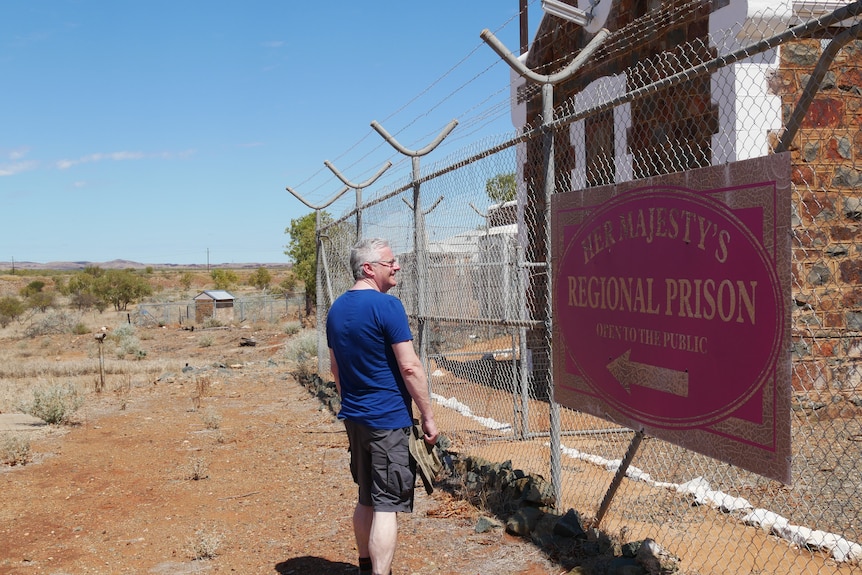 The man walks along the fence of Roebourne's old goal.