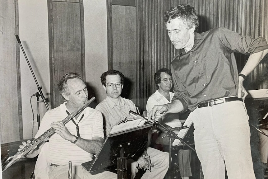 A black and white photo of a man playing the flute while a composer looks on.