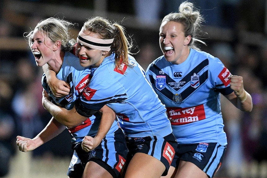 A rugby league player pumps her first and screams as she is hugged after scoring a try in the Women's State of Origin match.