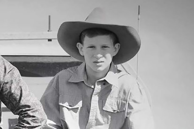 A young teenager in a hat sitting on the front of a four-wheel drive