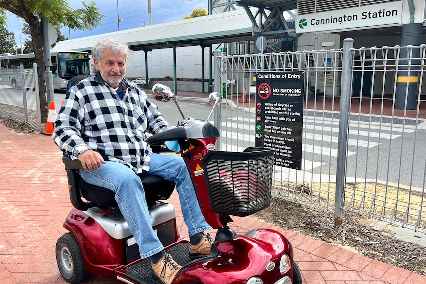 A man with grey hair sitting on a mobility scooter poses for a photo on a path across the road from Cannington station.