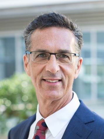 A middle-aged man with greying hair and square glasses smiles