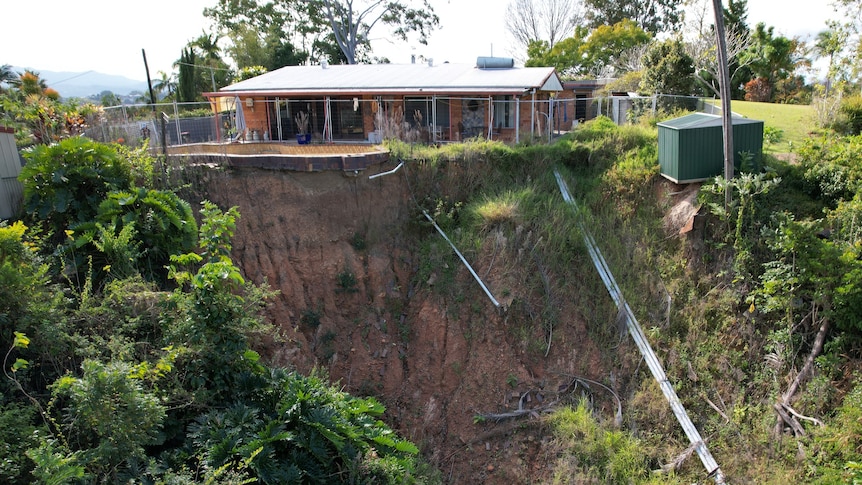 A brick house and concrete swimming pool teeter on the edge of a landslip 