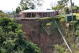 A brick house and concrete swimming pool teeter on the edge of a landslip 