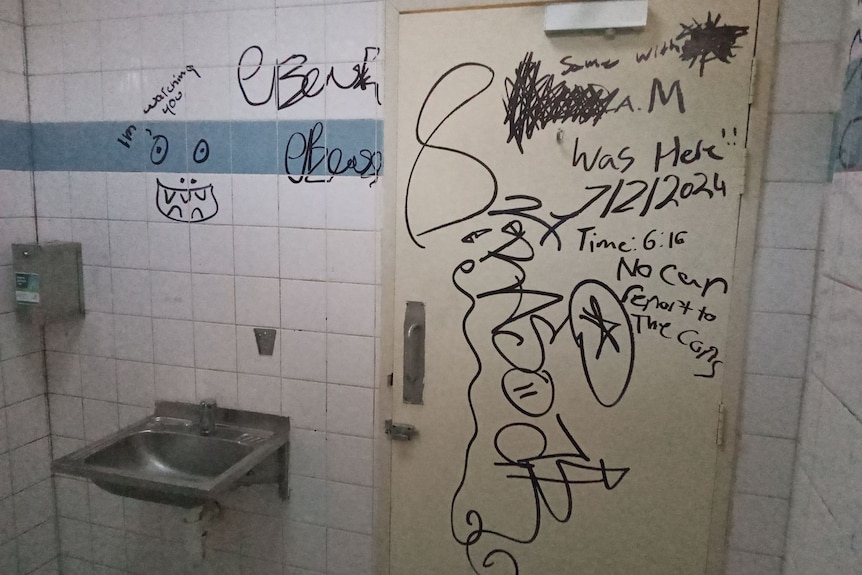 The inside of a public bathroom showing graffiti on the walls and door.