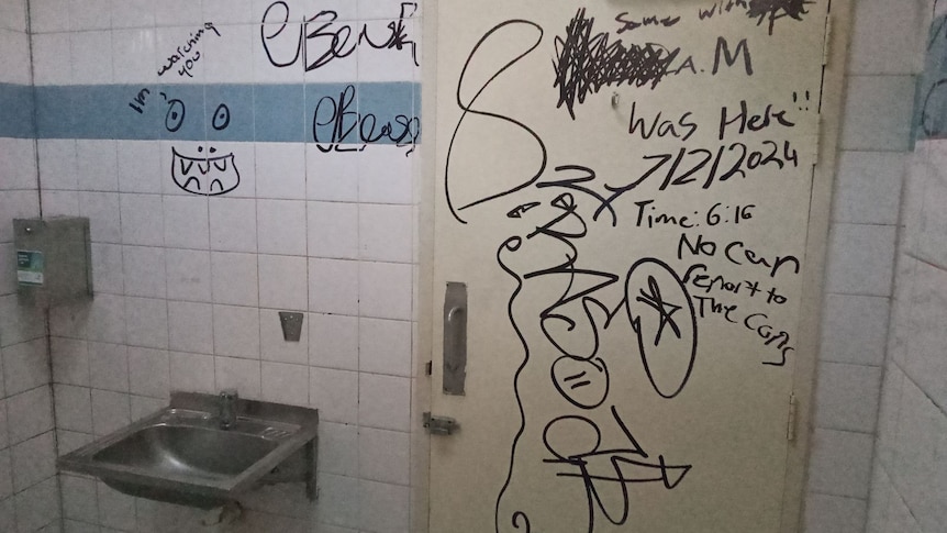 The inside of a public bathroom showing graffiti on the walls and door.
