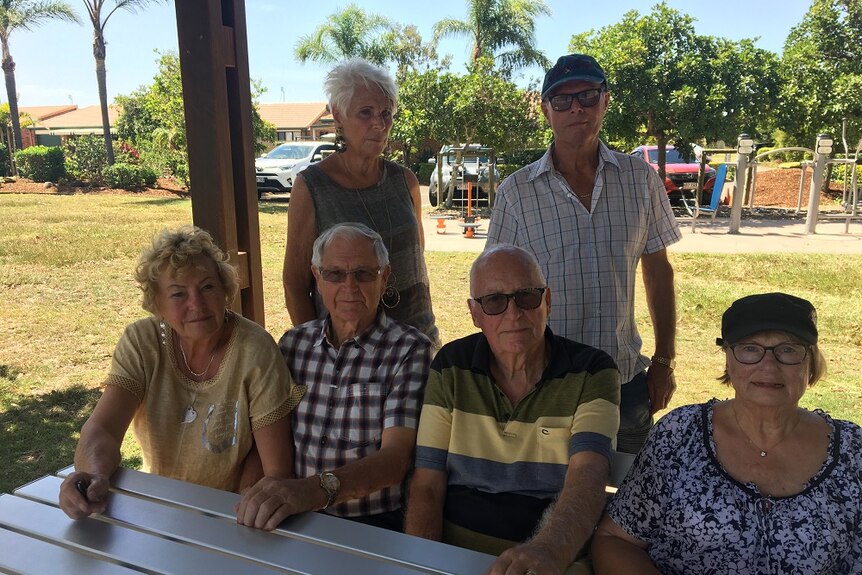 A group of older people gather outside around a picnic table