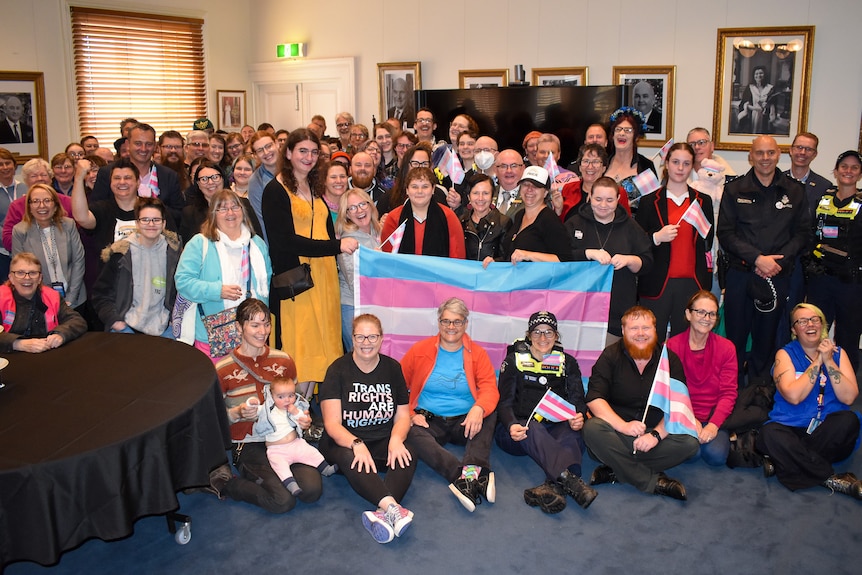 A group of people grin and hold a trans flag
