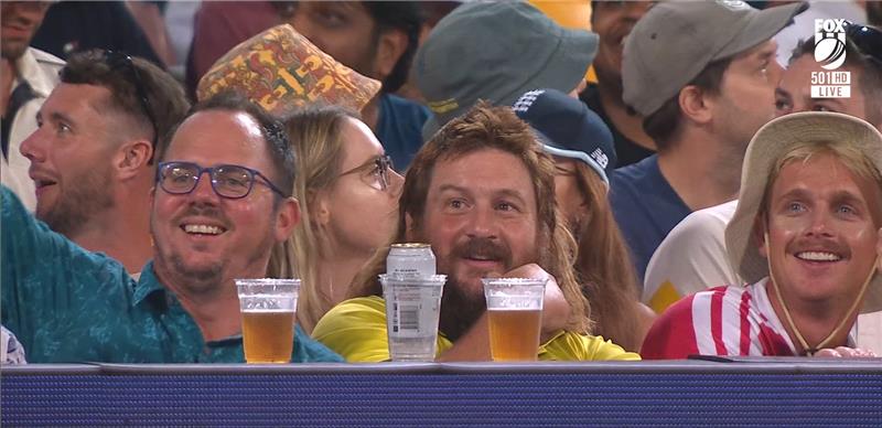 Un hombre con un salmonete parece avergonzado, con una cerveza delante en medio de una multitud de gente sonriente.