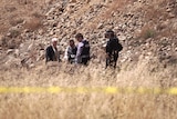 Five police officers look for clues at a rocky murder scene.