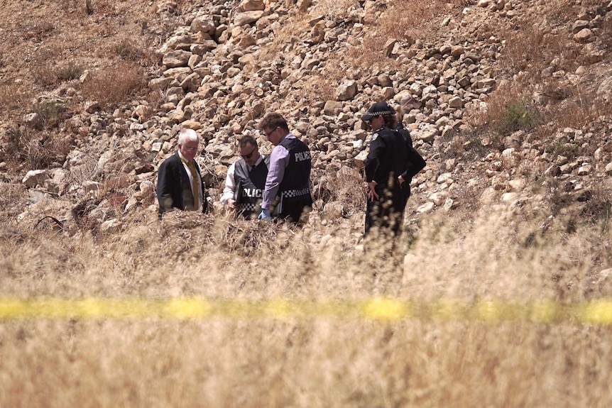 Five police officers look for clues at a rocky murder scene.