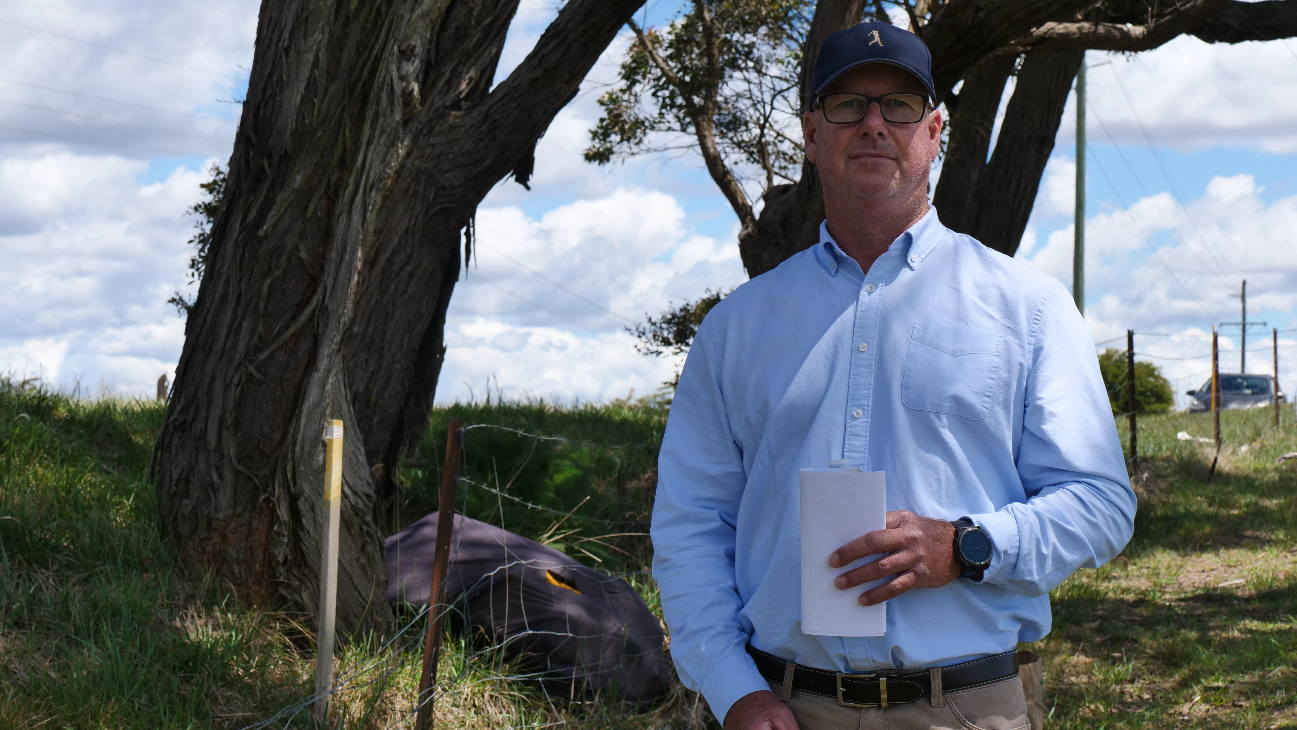 image of man in glasses and cap standing in front of trees