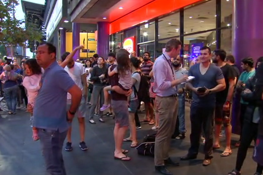 Dozens of people stand about on Spencer Street in Melbourne's CBD in dawn light.