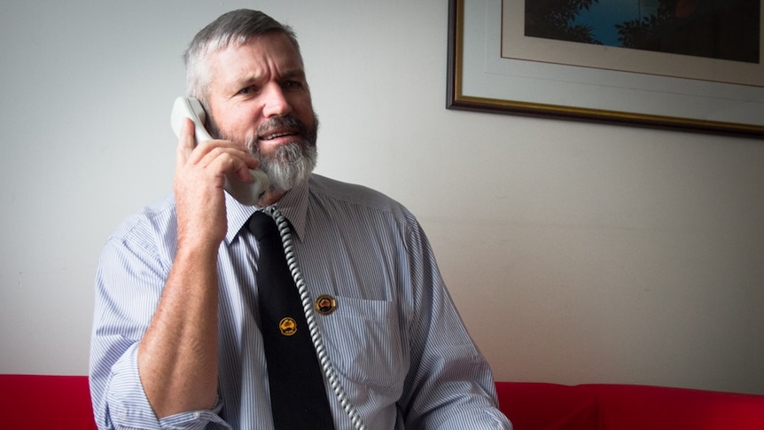 A seated man speaks into the handset of a landline telephone