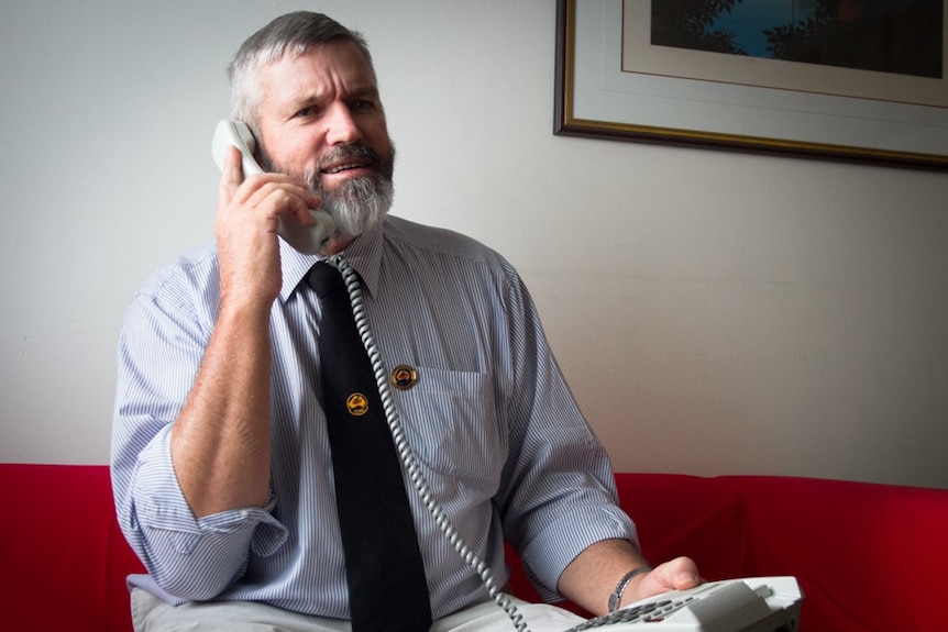 A seated man speaks into the handset of a landline telephone