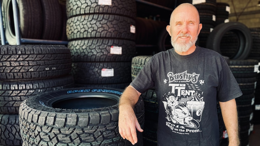 Man wearing a black shirt leans against a stack of tyres in front of a wall of tyres