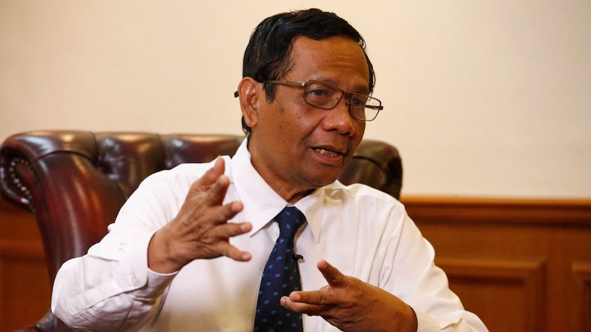 Indonesian man in white shirt and blue tie gestures with his hands as he speaks.