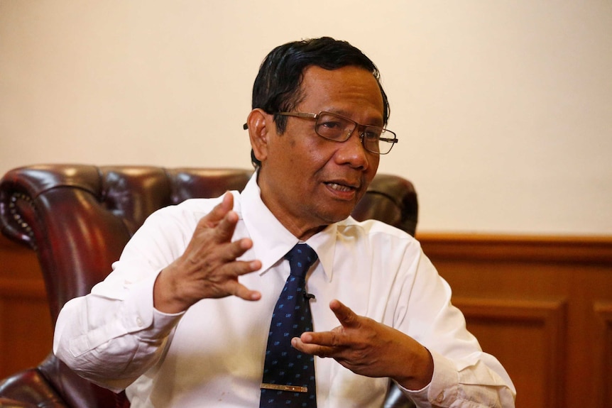 Indonesian man in white shirt and blue tie gestures with his hands as he speaks.