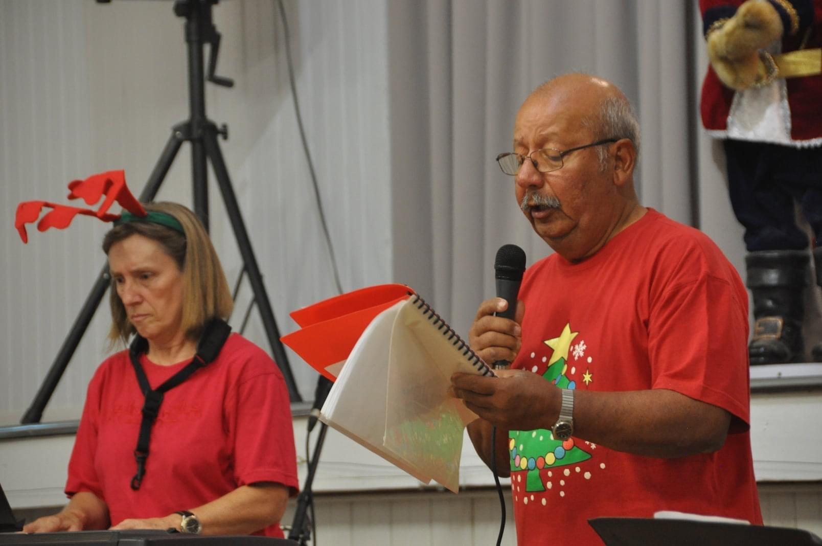 Woman in reindeer horns playing a keyboard, besides a man in a Christmas t-shirt singing into a microphone. 