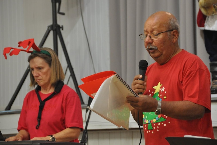 Woman in reindeer horns playing a keyboard, besides a man in a Christmas t-shirt singing into a microphone. 