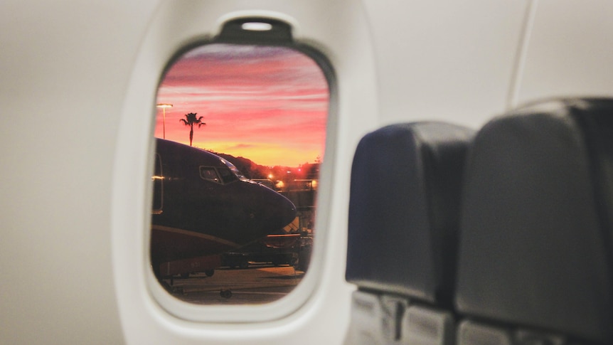 A window shows a pink sun set over an airplane.