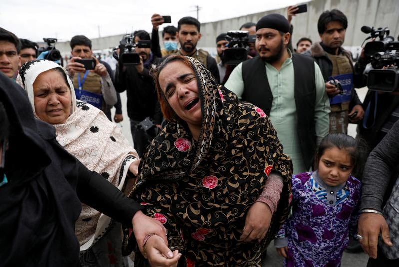 A woman crying with people and reporters in the background.
