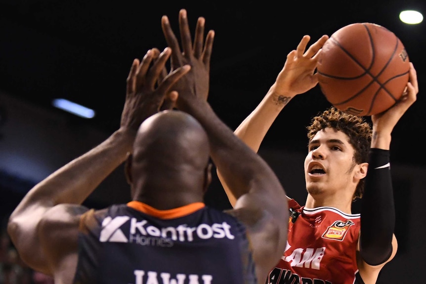 A basketball player gets ready to shoot the ball as a defender prepares to block him.