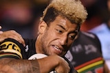 Viliame Kikau holds a rugby ball under his arm as two players in blue shirts try to tackle him