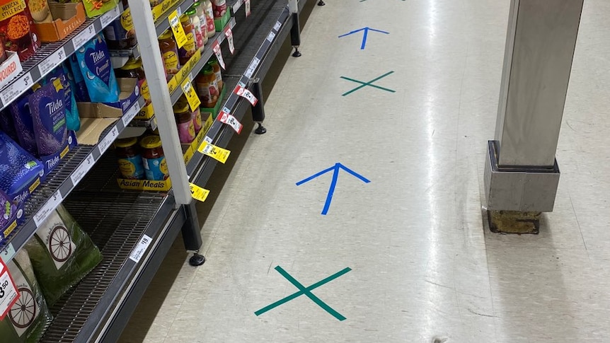 Blue arrows separate green crosses to indicate the spacing required for customers along the aisle of a supermarket.