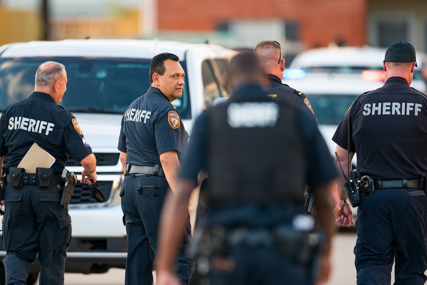 Sheriff looks over his shoulder, surrounded by other police officers at a crime scene.