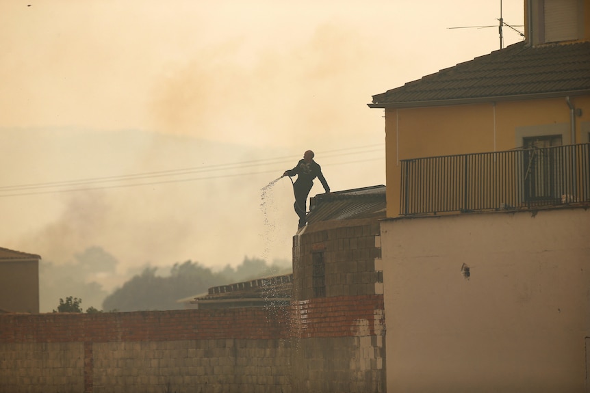 Un vicino distribuisce acqua per combattere il fuoco durante la seconda ondata di caldo dell'anno