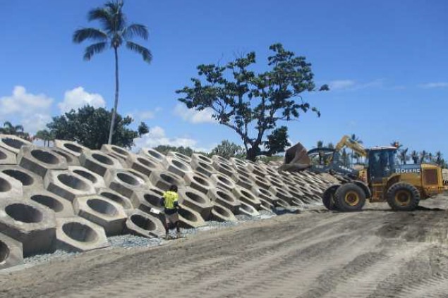 A worker stands looking at an excavator work on a concrete wall.