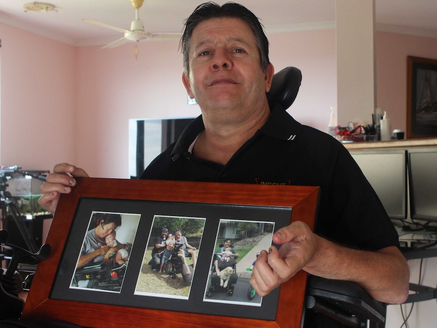 Mark Moodie holds a photo of his family as he sits in his apartment