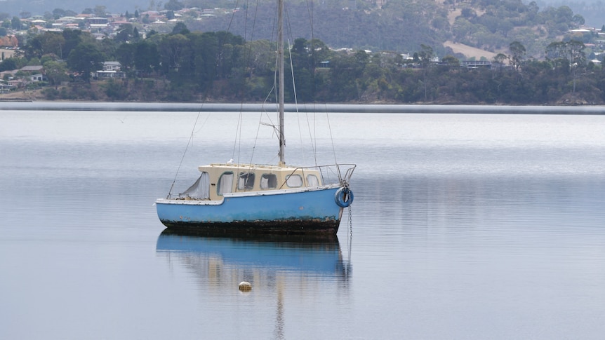 a small blue sailing boat oored on very still water